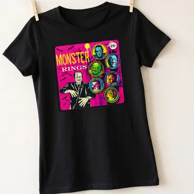 Vintage comic-style t-shirt featuring colorful monster faces and bold 'MONSTER RINGS' text — printed on a women's shirt
