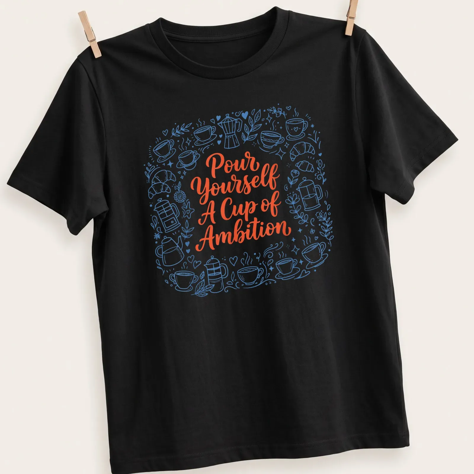 Whimsical coffee and croissants design with playful text in blue and orange — printed on a unisex t-shirt