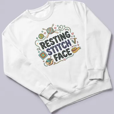 Colorful whimsical design featuring crochet yarn and knitting tools with text 'Resting Stitch Face' — printed on a unisex sweatshirt