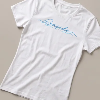Cursive script design featuring the word Seaside over wave imagery in blue and white — printed on a women's shirt
