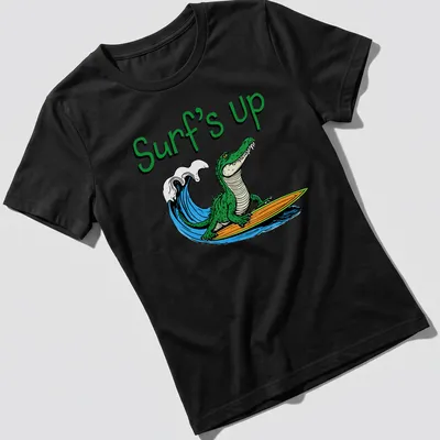 Cartoon alligator surfing with colorful text reading Surf's Up — printed on a women's shirt