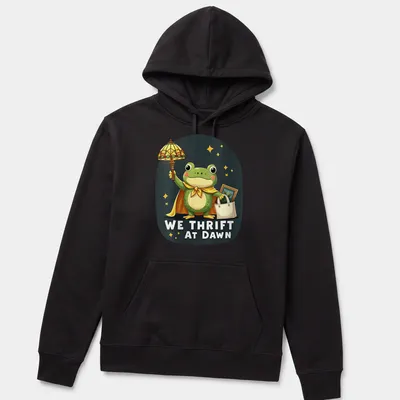 Kawaii frog cartoon holding a shopping bag with We Thrift At Dawn text — printed on a unisex hoodie